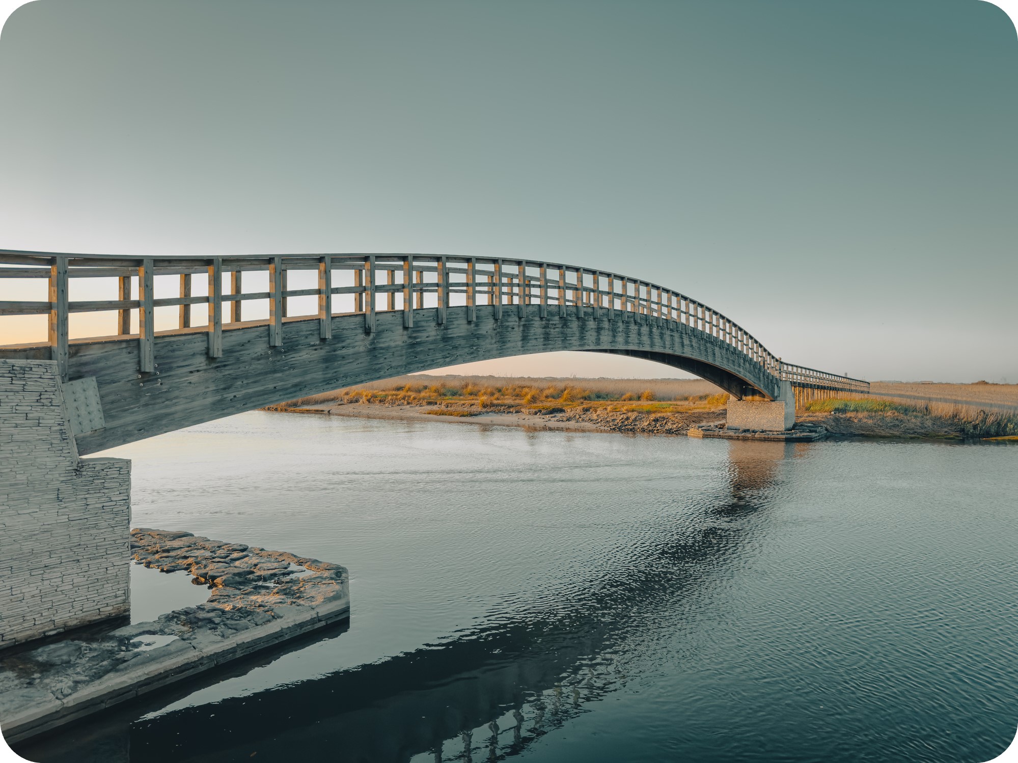 A beautiful wooden bridge reaching across a calm river.